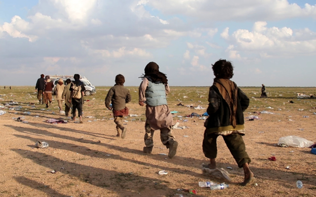 a group of boys walk in a row towards a vehicle. The ground is covered in litter and bottles.