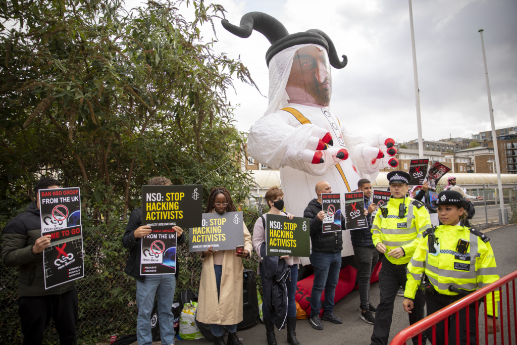A group of demonstrators stand in front of a blow up person, as they call for the NSO Group to stop hacking the phones of activists.