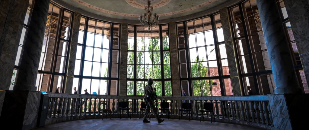 A Russian soldier patrols in front of wide tall windows in the Mariupol Philharmonic Hall..