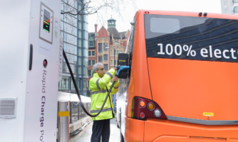 Bus driver charging electric bus which says 100% electric on the back window.