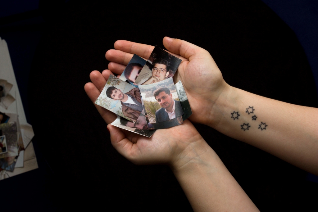 someone is holding a collection of images of people who have disappeared in Syria. The person has a star tattoo on their left hand.